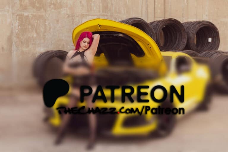 Yellow sports car with open hood featuring a woman with pink hair, tattoos, and black lingerie in an industrial setting.