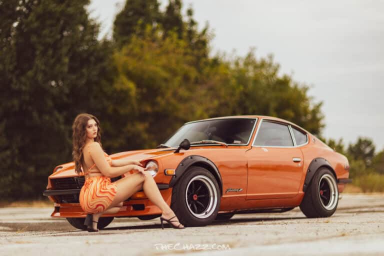 Orange vintage Datsun 240Z sports car with black wheel arches and a woman in a matching orange dress posing beside it.