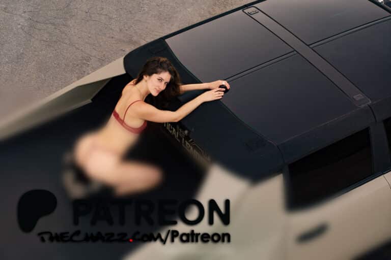 Young woman in red lingerie lying on car roof, looking up at camera from above.
