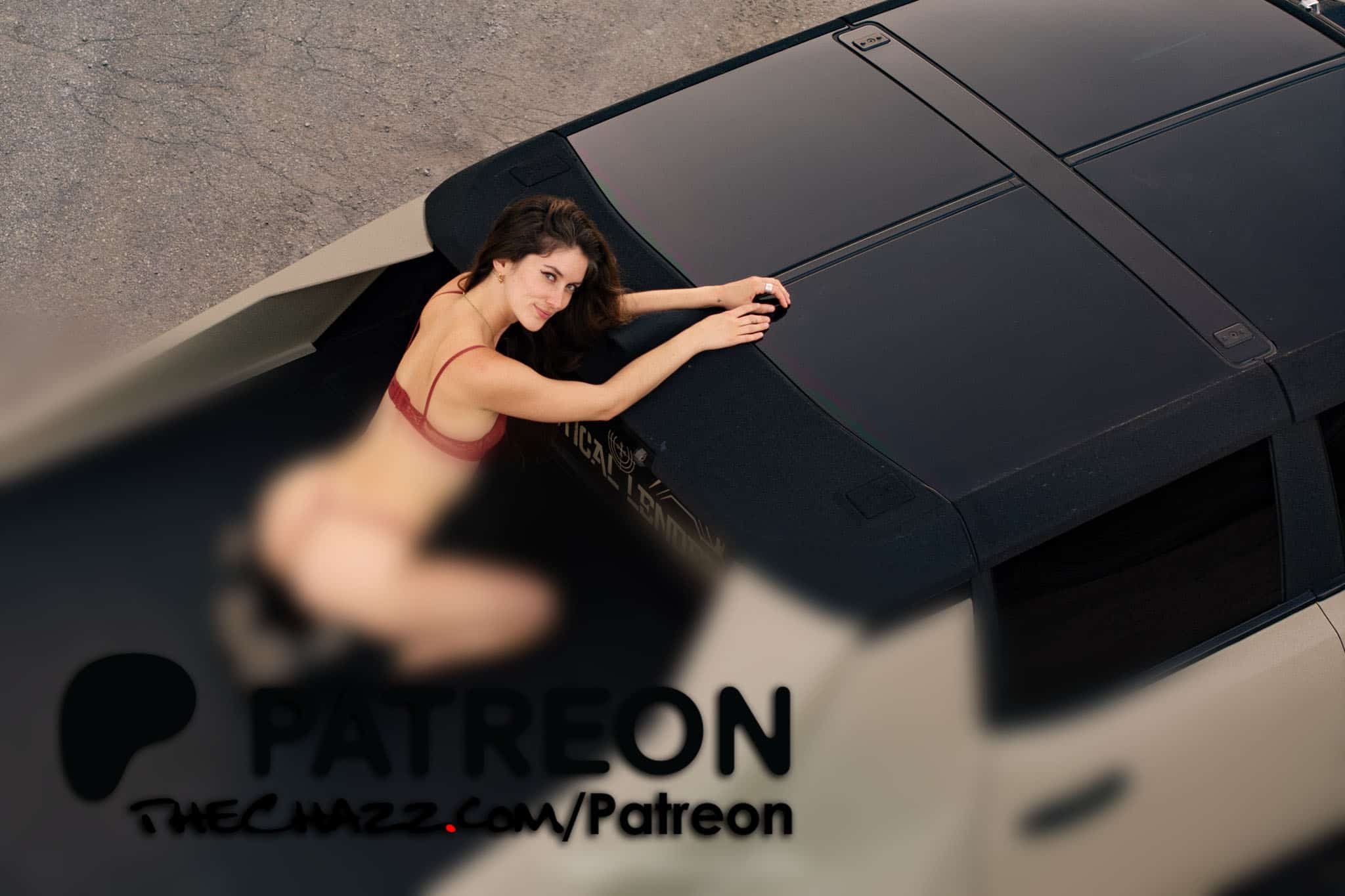 Young woman in red lingerie lying on car roof, looking up at camera from above.