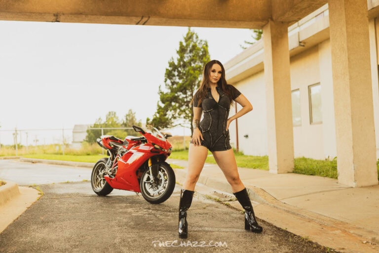 Alisa posing with a red Ducati motorcycle in a black romper and boots.