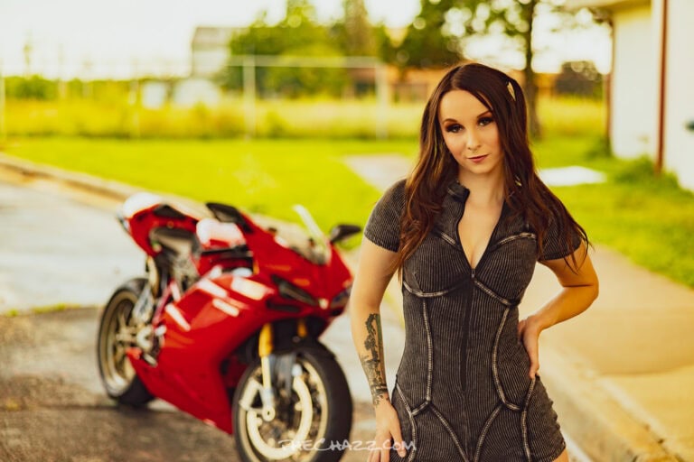 Alisa posing with a red Ducati motorcycle in a black romper and boots.