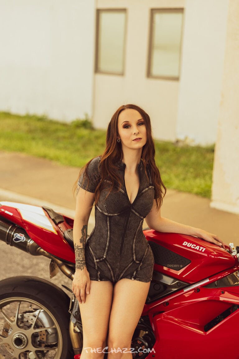 Alisa posing with a red Ducati motorcycle in a black romper and boots.
