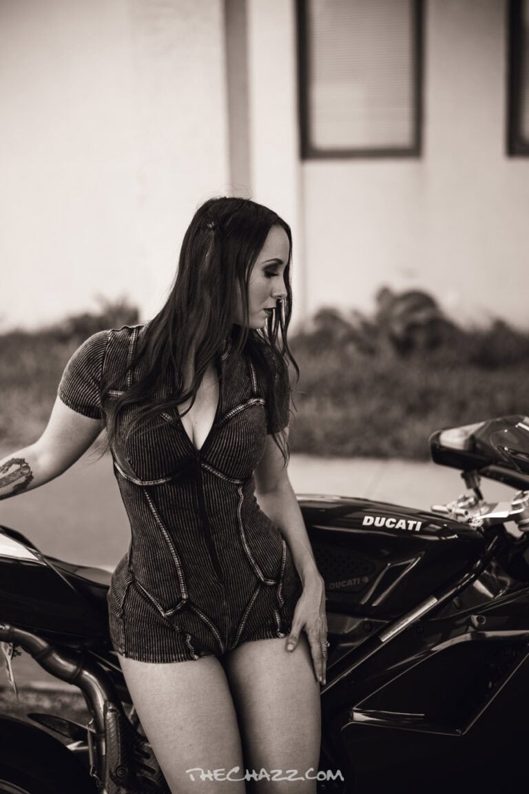 Alisa posing with a red Ducati motorcycle in a black romper and boots.
