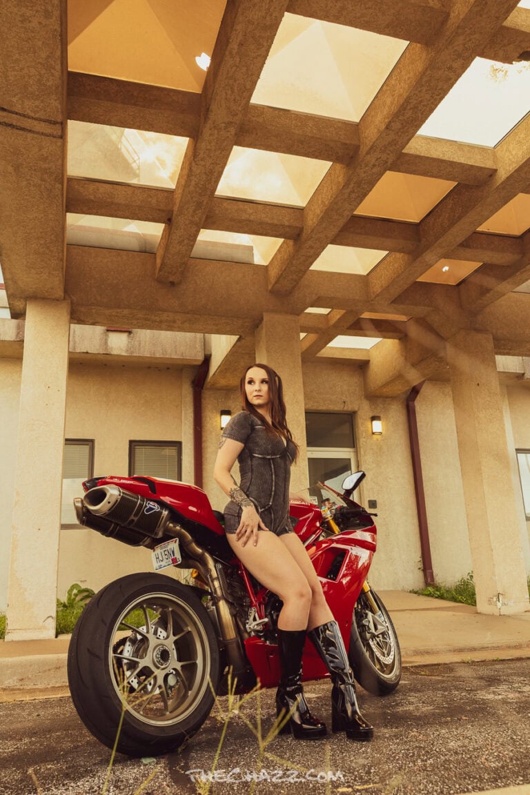 Alisa posing with a red Ducati motorcycle in a black romper and boots.