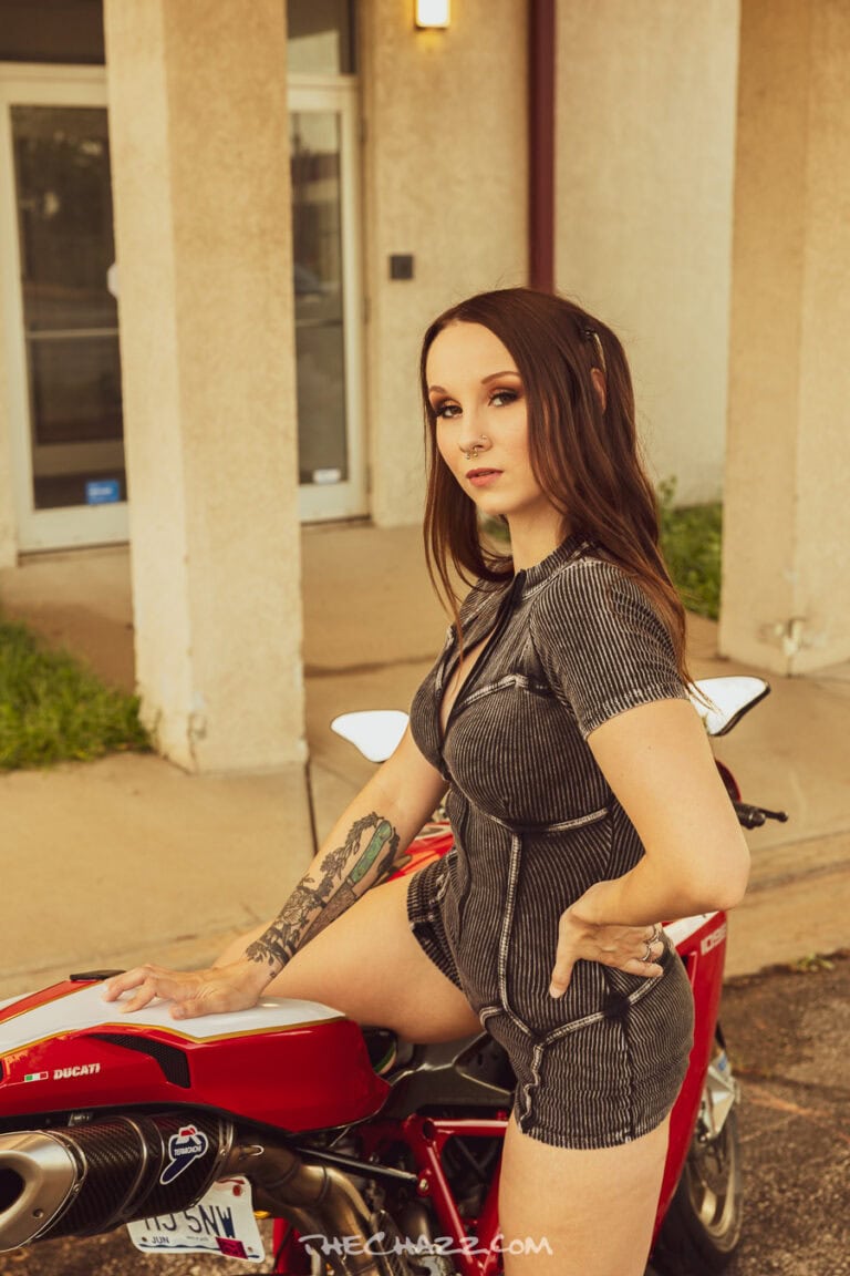 Alisa posing with a red Ducati motorcycle in a black romper and boots.