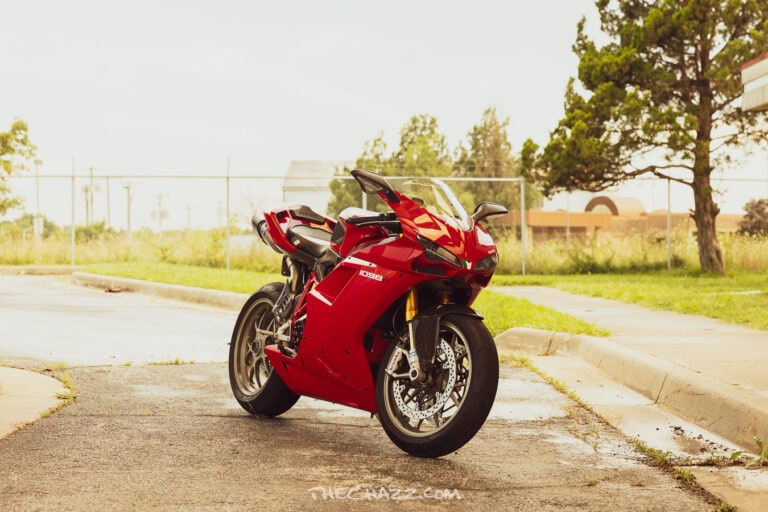Alisa posing with a red Ducati motorcycle in a black romper and boots.